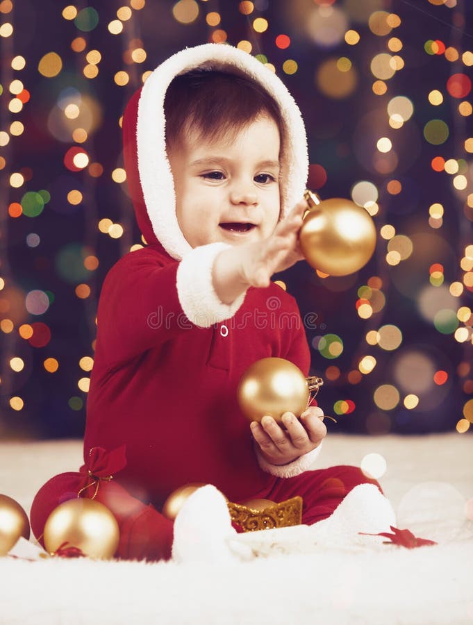 El muchacho del pequeño niño vestido como santa que juega con la decoración de la Navidad, el fondo oscuro con la iluminación y e fotografía de archivo libre de regalías El muchacho del pequeño niño vestido como santa que juega con la decoración de la Navidad, el fondo oscuro con la iluminación y e fotografía de archivo libre de regalías
