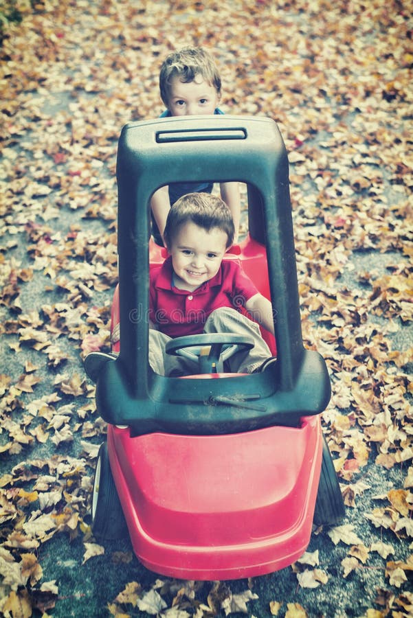 El muchacho empuja su Brother en Toy Car Outside imagenes de archivo El muchacho empuja su Brother en Toy Car Outside imagenes de archivo