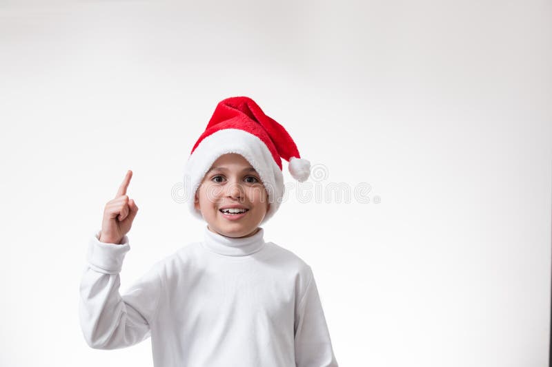 El muchacho en las sonrisas y los puntos rojos del sombrero de santa el dedo hacia arriba. Concepto de Navidad fotos de archivo libres de regalías