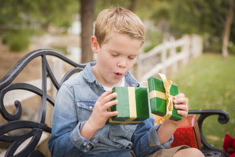El muchacho joven sorprendido abre el regalo de la Navidad afuera imagen de archivo libre de regalías El muchacho joven sorprendido abre el regalo de la Navidad afuera imagen de archivo libre de regalías
