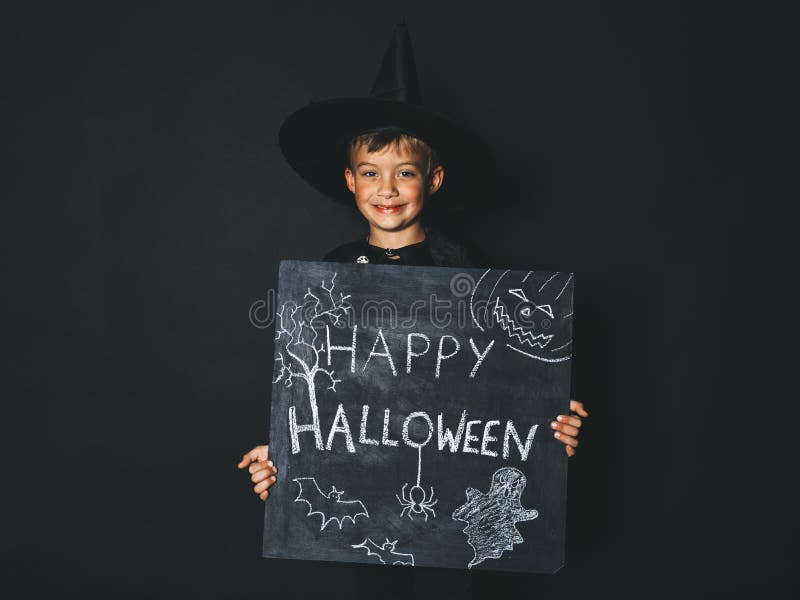 El muchacho joven vestido como mago está sosteniendo la pizarra del feliz Halloween fotos de archivo El muchacho joven vestido como mago está sosteniendo la pizarra del feliz Halloween fotos de archivo