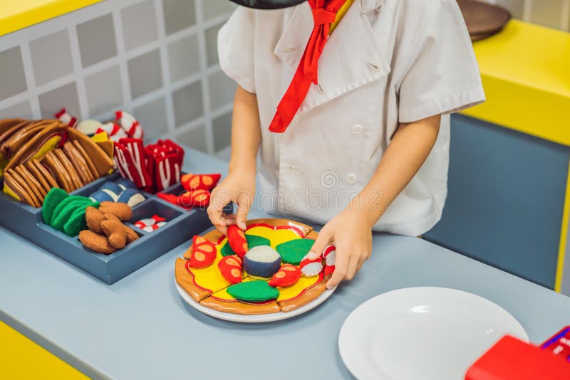 El muchacho juega en la cocina del juguete, cocina una pizza foto de archivo El muchacho juega en la cocina del juguete, cocina una pizza foto de archivo