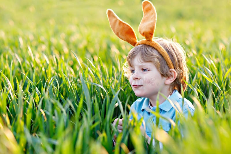 El muchacho lindo del niño con los oídos del conejito que se divierten con los huevos de Pascua tradicionales caza en día soleado fotos de archivo libres de regalías El muchacho lindo del niño con los oídos del conejito que se divierten con los huevos de Pascua tradicionales caza en día soleado fotos de archivo libres de regalías
