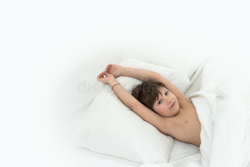 El muchacho miente en una cama en las ropas de cama blancas deslizar al niño