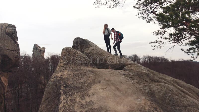 El muchacho y la muchacha atléticos con un turista hace excursionismo subir la montaña rocosa, después conseguir en el top, lleva