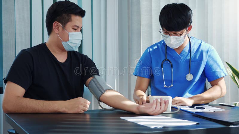 El médico asiático está utilizando un monitor de la presión arterial de los pacientes en el momento de su revisión anual y explica imagenes de archivo