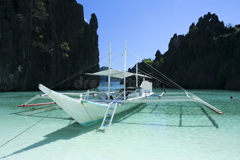 Tradiční filipínské banky outrigger lodi uprostřed krasové skalní útvary v jasné modré vody el nido ostrově palawan na filipínách.