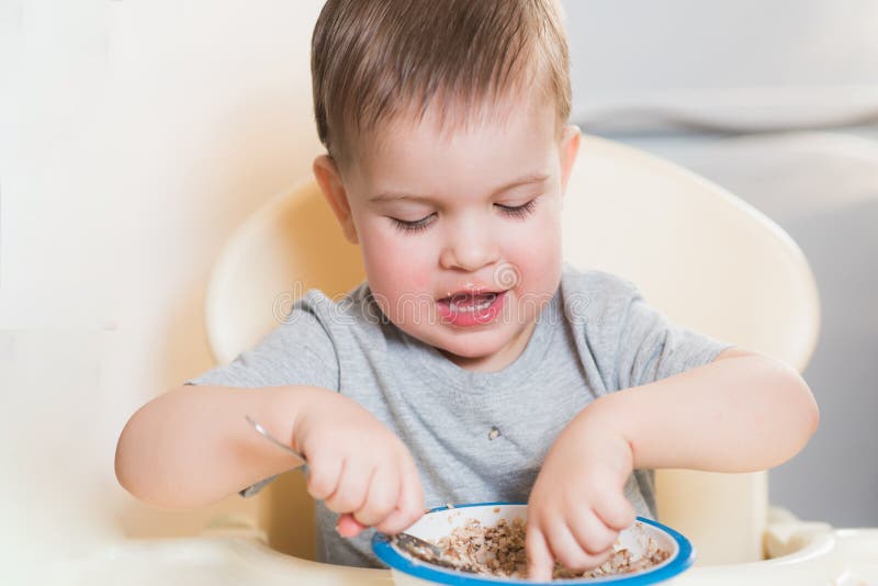El niño come las gachas de avena del alforfón en la cocina fotos de archivo libres de regalías El niño come las gachas de avena del alforfón en la cocina fotos de archivo libres de regalías
