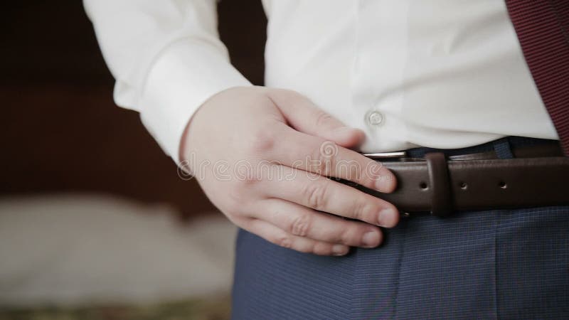 El novio pone la correa en sus pantalones en mañana de la boda