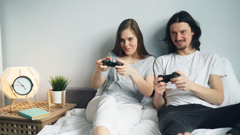 El novio y la novia jovenes lindos de los pares están jugando el videojuego en cama en casa