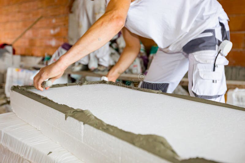 View on worker's hand with trowel, applying glue on thermal insulation material, Styrofoam for insulation the building under construction. View on worker's hand with trowel, applying glue on thermal insulation material, Styrofoam for insulation the building under construction