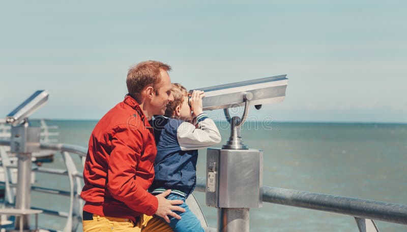 El padre ayuda a su pequeño hijo a mirar en prismáticos del mar fotografía de archivo libre de regalías El padre ayuda a su pequeño hijo a mirar en prismáticos del mar fotografía de archivo libre de regalías