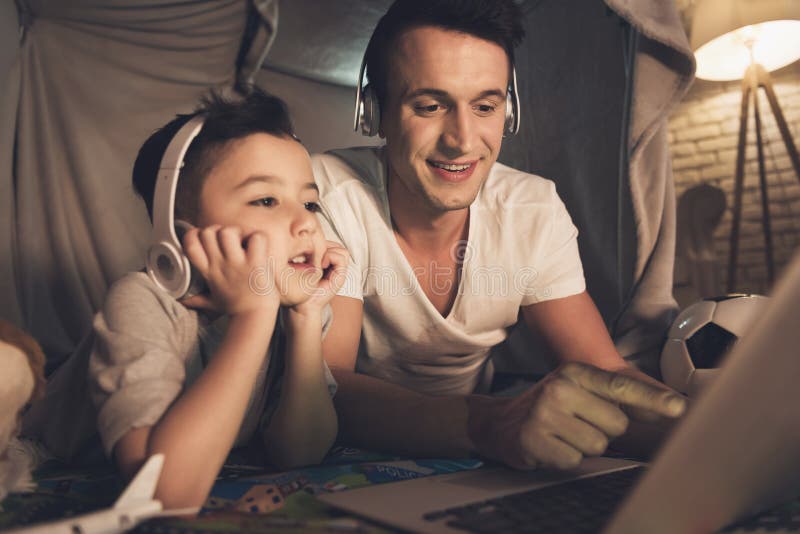 El padre y el hijo están hablando en Skype con la familia en el ordenador portátil en la noche en casa foto de archivo El padre y el hijo están hablando en Skype con la familia en el ordenador portátil en la noche en casa foto de archivo