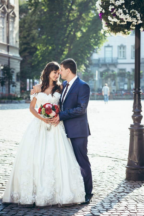 El par atractivo feliz del recién casado es suavemente de abrazo y de tacto de narices en la calle soleada Retrato integral fotos de archivo libres de regalías El par atractivo feliz del recién casado es suavemente de abrazo y de tacto de narices en la calle soleada Retrato integral fotos de archivo libres de regalías