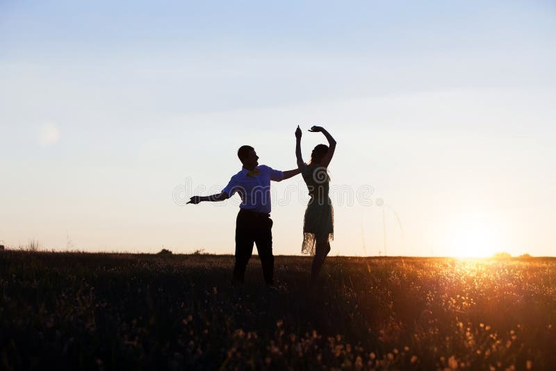 Siluetas de una joven pareja bailando en el campo imagen de archivo libre de regalías