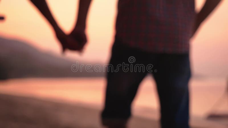 El par romántico camina en la playa en la puesta del sol asombrosa que lleva a cabo las manos Pares jovenes felices que disfrutan almacen de metraje de vídeo