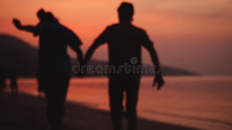 El par romántico camina en la playa tropical en la puesta del sol asombrosa que lleva a cabo las manos Pares jovenes felices que almacen de video