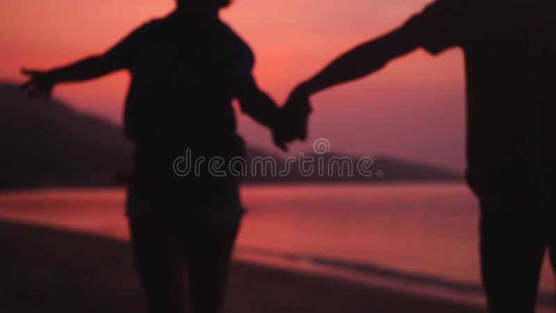 El par romántico corre en la playa en la puesta del sol asombrosa que lleva a cabo las manos Pares jovenes felices que disfrutan almacen de video