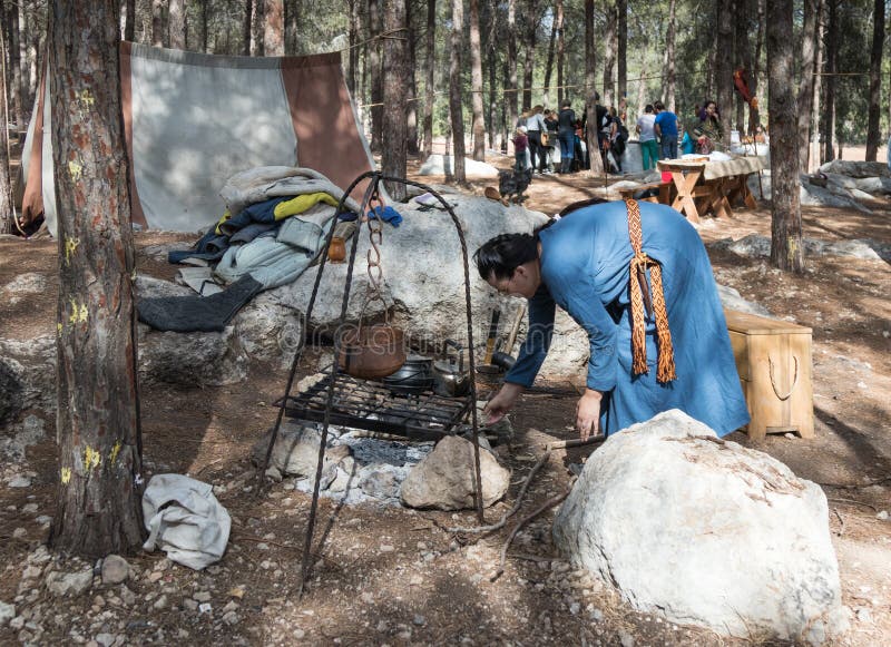 El participante de la reconstrucción del ` de Viking Village del ` enciende un fuego en el hogar en el campo en el bosque cerca d foto de archivo libre de regalías El participante de la reconstrucción del ` de Viking Village del ` enciende un fuego en el hogar en el campo en el bosque cerca d foto de archivo libre de regalías