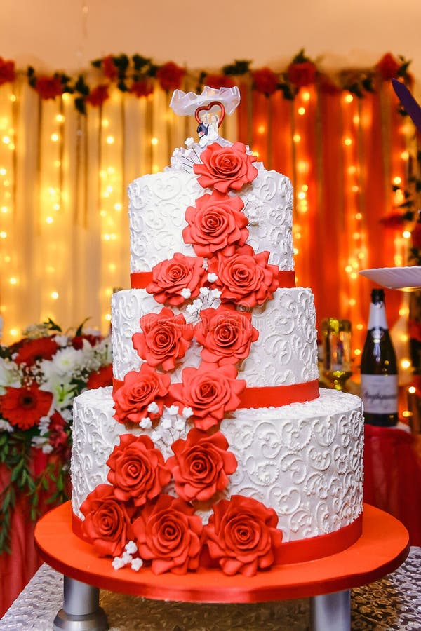 El pastel de bodas blanco del tres-piso con las flores rojas fotografía de archivo El pastel de bodas blanco del tres-piso con las flores rojas fotografía de archivo