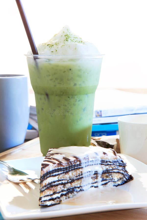 El pedazo de torta mable con crema de la vainilla y refresca té verde en gla fotografía de archivo