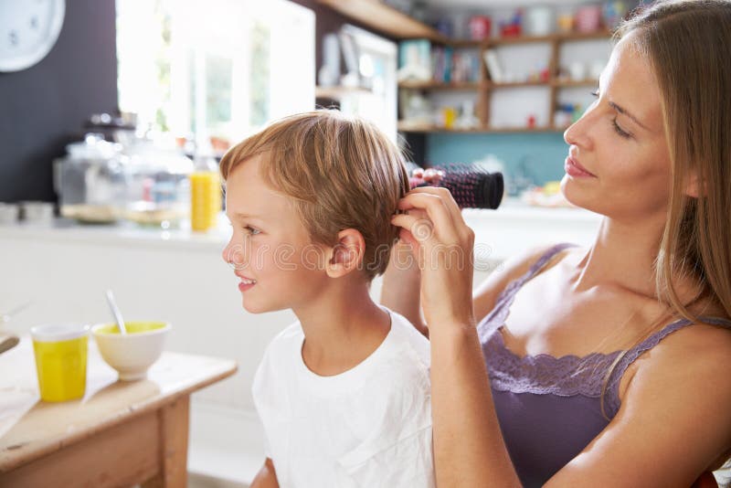 El pelo del hijo de cepillado de la madre en la mesa de desayuno fotografía de archivo El pelo del hijo de cepillado de la madre en la mesa de desayuno fotografía de archivo