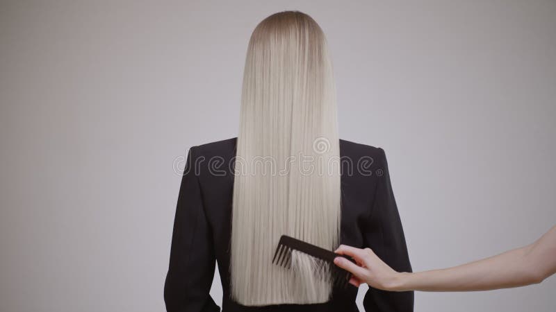 El peluquero peina el pelo largo de una mujer rubia vista trasera. metrajes