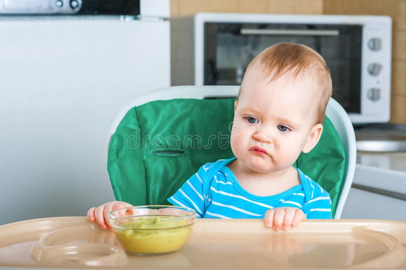 El pequeño bebé no quiere comer primero comida complementaria. niño disgustado en la trona