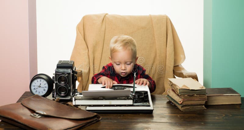 El pequeño niño escribe el documento a máquina sobre la máquina de escribir retra en el escritorio El muchacho escribe llaves a m fotografía de archivo El pequeño niño escribe el documento a máquina sobre la máquina de escribir retra en el escritorio El muchacho escribe llaves a m fotografía de archivo