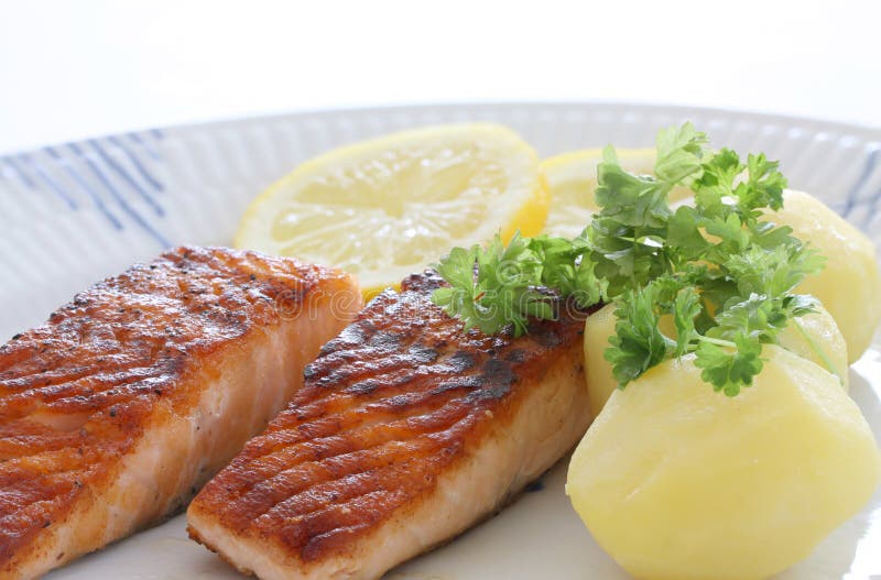 El pescado de color salm?n asado a la parrilla corta en una placa con las patatas, el perejil y las rebanadas de lim?n E fotografía de archivo libre de regalías El pescado de color salm?n asado a la parrilla corta en una placa con las patatas, el perejil y las rebanadas de lim?n E fotografía de archivo libre de regalías