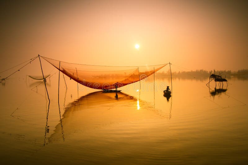 El pescador no identificado comprueba sus redes en madrugada en el río en Hoian, Vietnam imagenes de archivo
