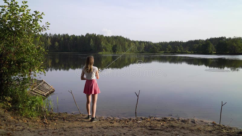 El pescador rubio de la chica joven está pescando en el lago del bosque en el verano La mujer atractiva en vestido corto aprende almacen de video
