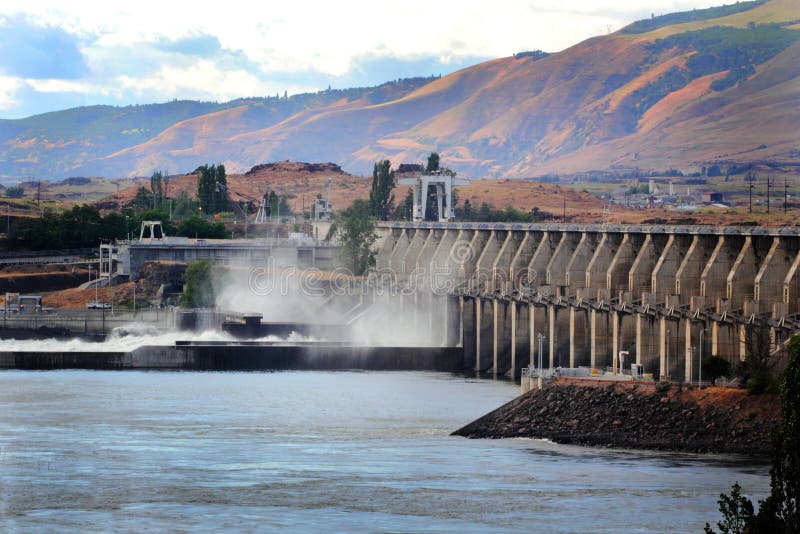 The Dalles Dam on the Columbia River with territorial view of the Washington hills under white fluffy clouds overhead. The Dalles Dam on the Columbia River with territorial view of the Washington hills under white fluffy clouds overhead.