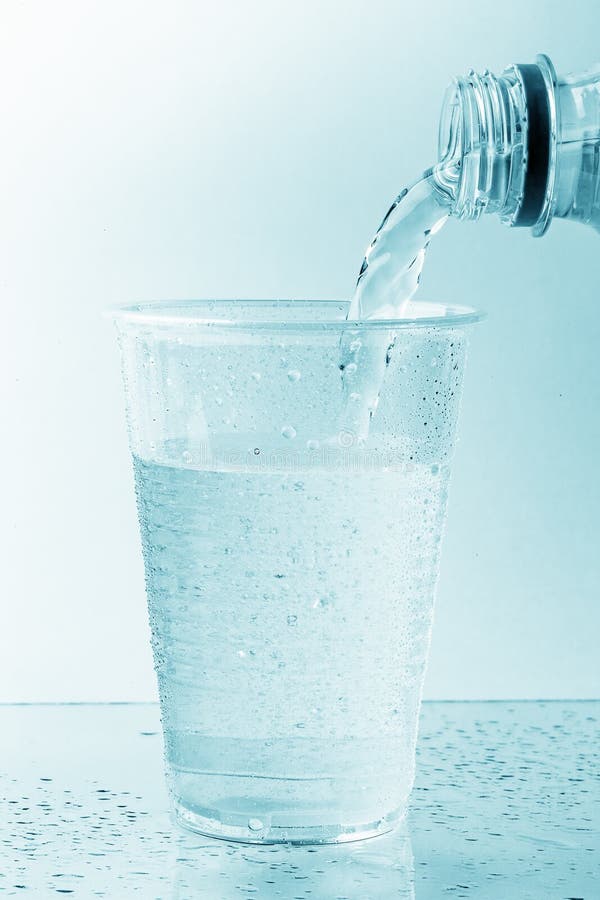 El poner mala cara del agua mineral pura de la botella plástica en el vidrio o la taza transparente imagen de archivo El poner mala cara del agua mineral pura de la botella plástica en el vidrio o la taza transparente imagen de archivo