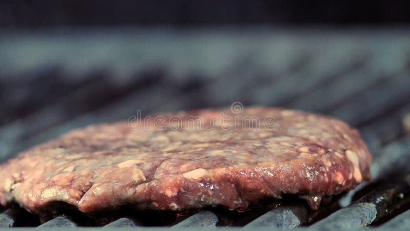 El primer de una empanada redonda de la hamburguesa se asa a la parrilla y el humo ligero va fotografía de archivo El primer de una empanada redonda de la hamburguesa se asa a la parrilla y el humo ligero va fotografía de archivo