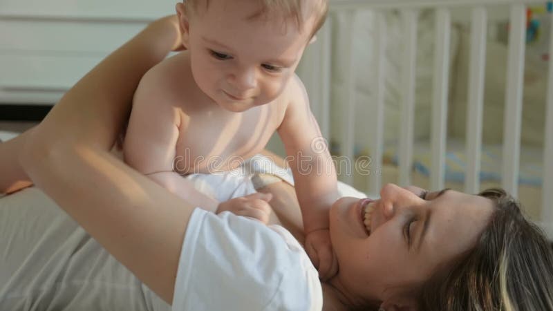 El primer tiró de la madre joven feliz que se divertía con su hijo del bebé en cama en el dormitorio