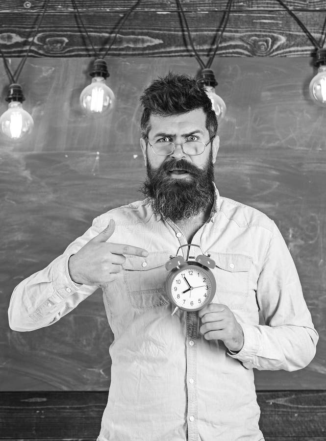 El profesor en lentes sostiene el despertador Horario y concepto del r?gimen El inconformista barbudo sostiene el reloj, pizarra imágenes de archivo libres de regalías El profesor en lentes sostiene el despertador Horario y concepto del r?gimen El inconformista barbudo sostiene el reloj, pizarra imágenes de archivo libres de regalías