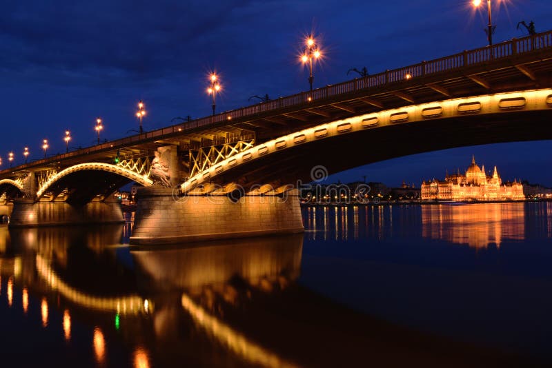 Margaret bridge in Budapest, Hungary at blue hour. perspective view with the Parliament under the arches. brightly illuminated steel arches and lights. beautiful reflections on the water. tourism and travel. European destinations concept. transportation and structural design. Margaret bridge in Budapest, Hungary at blue hour. perspective view with the Parliament under the arches. brightly illuminated steel arches and lights. beautiful reflections on the water. tourism and travel. European destinations concept. transportation and structural design.