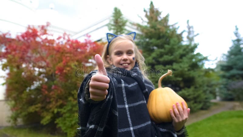 El pulgar alegre de la demostración de la muchacha para arriba, sostiene la calabaza de Jack para Halloween, día de fiesta del ot imagenes de archivo El pulgar alegre de la demostración de la muchacha para arriba, sostiene la calabaza de Jack para Halloween, día de fiesta del ot imagenes de archivo