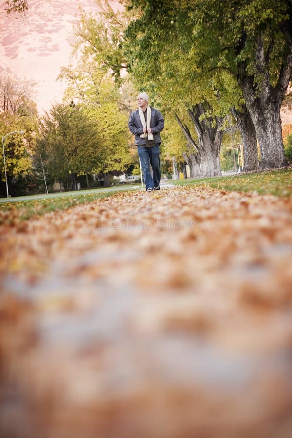 Young man dressed in cooler clothes walks along the sidewalk, which is covered with leaves. Young man dressed in cooler clothes walks along the sidewalk, which is covered with leaves