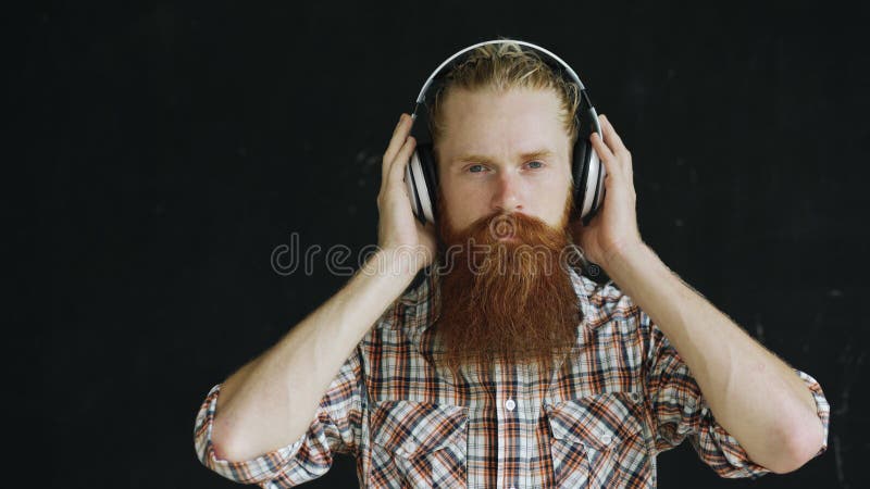 El retrato del primer del hombre joven barbudo en auriculares escucha la música y la mirada en la sonrisa de la cámara fotografía de archivo libre de regalías El retrato del primer del hombre joven barbudo en auriculares escucha la música y la mirada en la sonrisa de la cámara fotografía de archivo libre de regalías