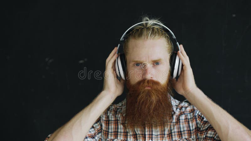El retrato del primer del hombre joven barbudo en auriculares escucha la música y la mirada en la sonrisa de la cámara imágenes de archivo libres de regalías El retrato del primer del hombre joven barbudo en auriculares escucha la música y la mirada en la sonrisa de la cámara imágenes de archivo libres de regalías