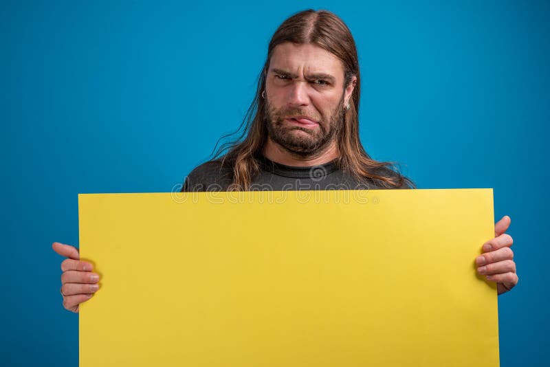 El retrato del varón adulto que hace una mueca divertida visible mientras que lleva a cabo un amarillo hace publicidad de la band imagenes de archivo El retrato del varón adulto que hace una mueca divertida visible mientras que lleva a cabo un amarillo hace publicidad de la band imagenes de archivo