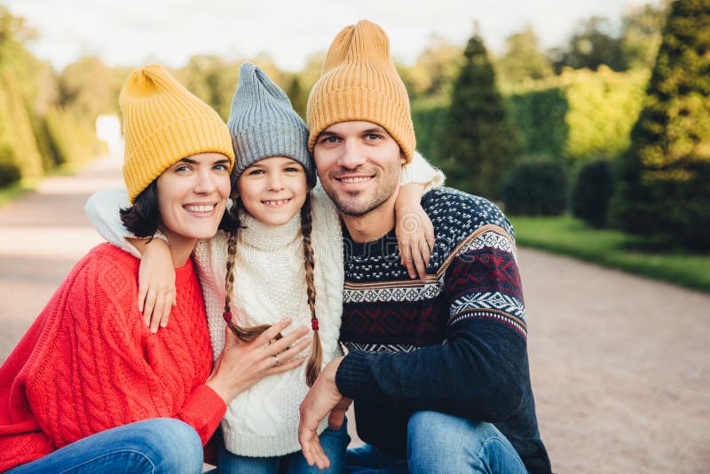 El retrato horizontal del abrazo cariñoso amistoso de la familia, los casquillos y los suéteres hechos punto desgaste, camina jun foto de archivo El retrato horizontal del abrazo cariñoso amistoso de la familia, los casquillos y los suéteres hechos punto desgaste, camina jun foto de archivo