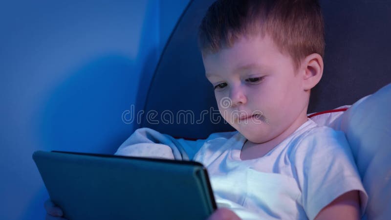 El rostro de los niños es iluminado por la luz de la noche portátil el tiempo libre en casa. lindo chico rubio caucásico en la noc almacen de metraje de vídeo