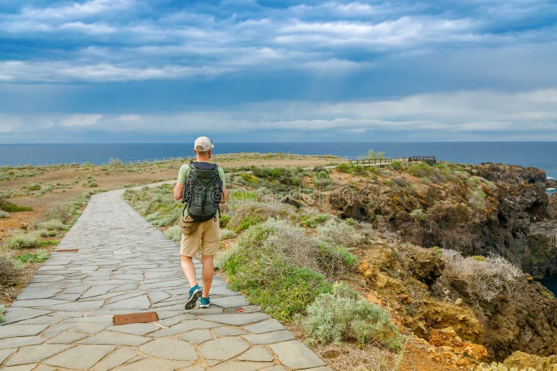El Sauzal Tenerife酒店的独行旅客背着背包，沿着石砌的路径步行，拥有茂密的崎岖的悬崖边 库存图片