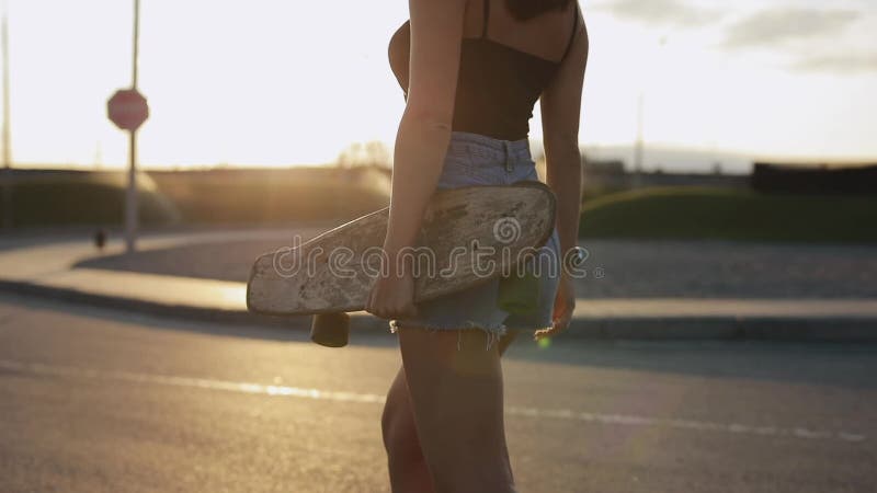 El skater de la mujer lleva su monopatín en manos en la puesta del sol