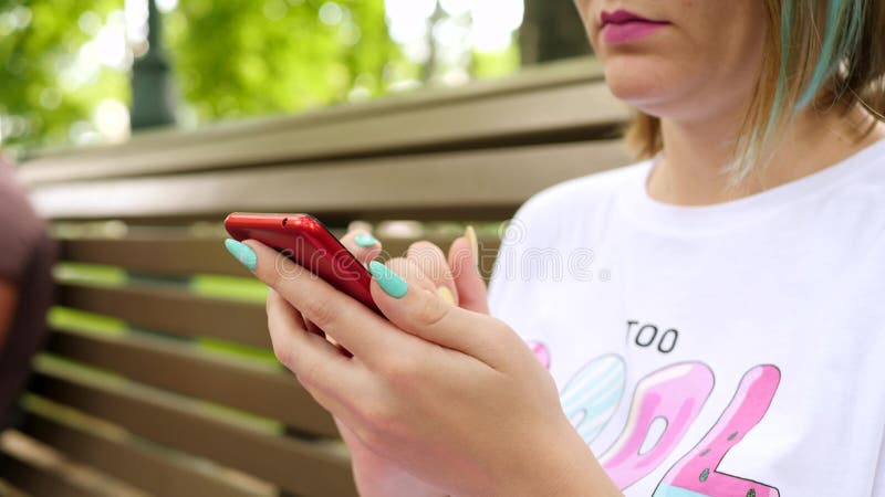 El smartphone del uso de la mujer se sienta en banco en parque del verano