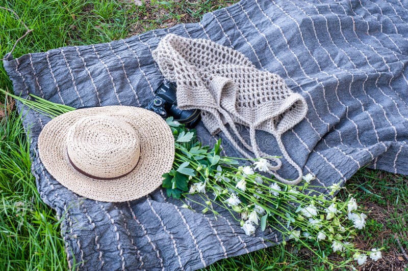 El sombrero de paja amarillo, el ramo de las flores, una cámara y el bolso hecho punto pone en la estera gris en la hierba al air fotografía de archivo libre de regalías El sombrero de paja amarillo, el ramo de las flores, una cámara y el bolso hecho punto pone en la estera gris en la hierba al air fotografía de archivo libre de regalías