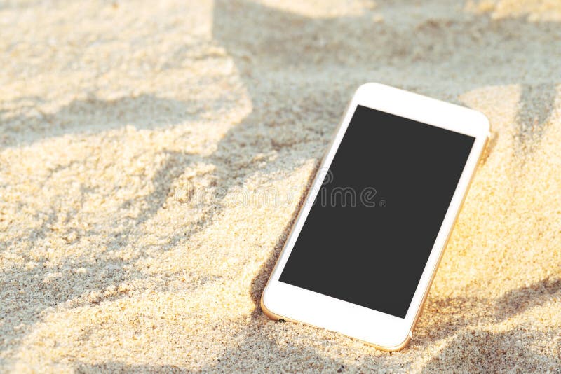El teléfono elegante móvil puso descenso en la playa tropical de la arena con el fondo de la textura de la luz del sol espacio ne fotografía de archivo El teléfono elegante móvil puso descenso en la playa tropical de la arena con el fondo de la textura de la luz del sol espacio ne fotografía de archivo